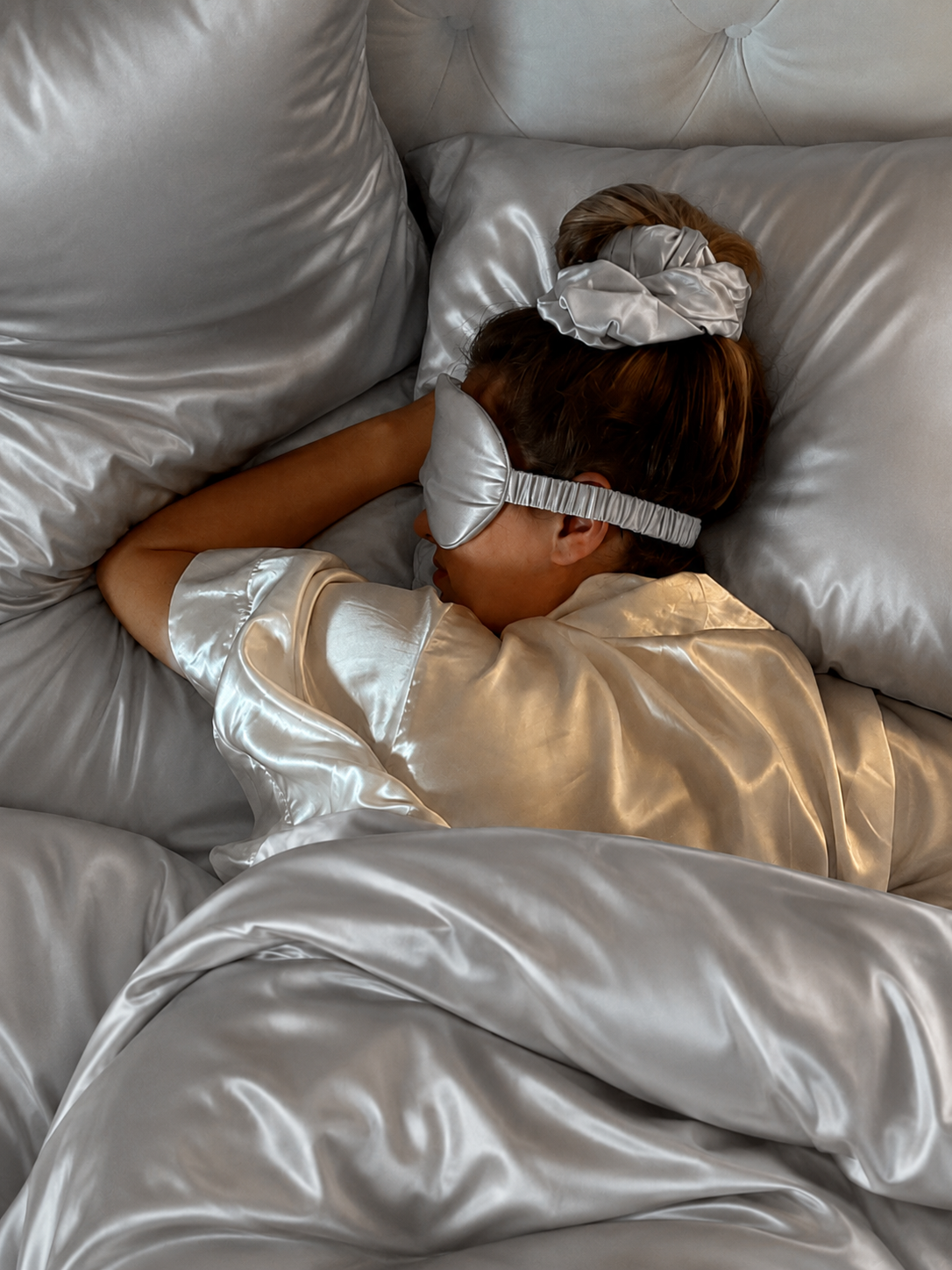 Woman sleeping in a Platinum Silver silk sleep mask, scrunchie and pyjamas