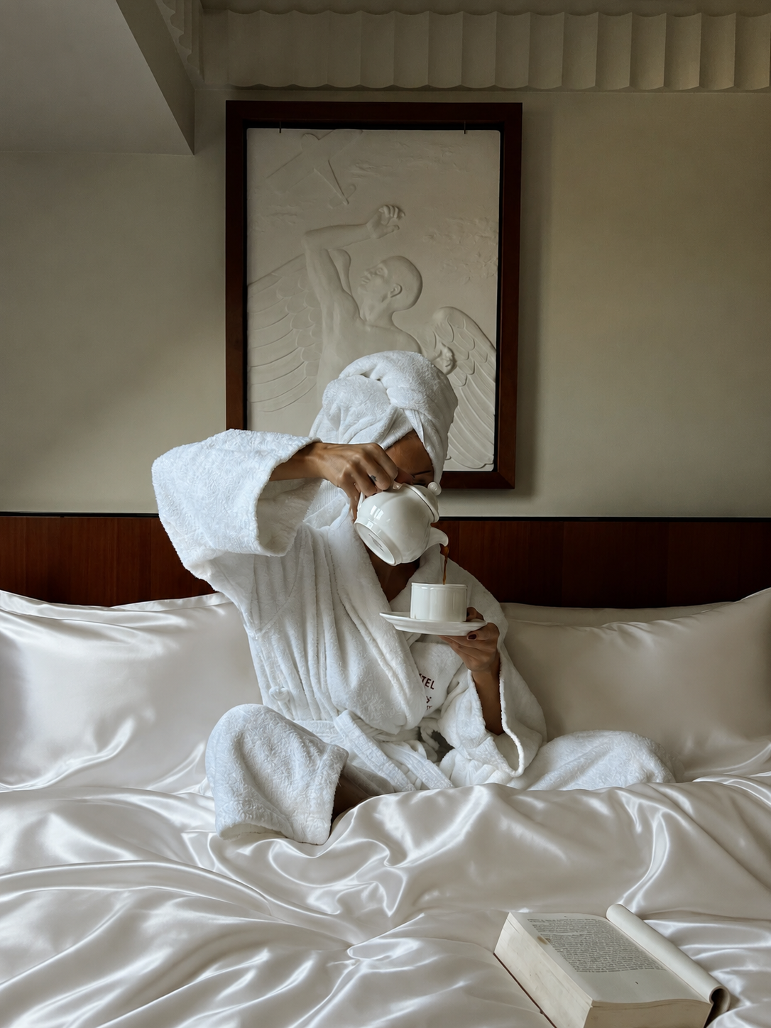Woman in a bathrobe pouring tea while sitting on Pearl White silk bedding