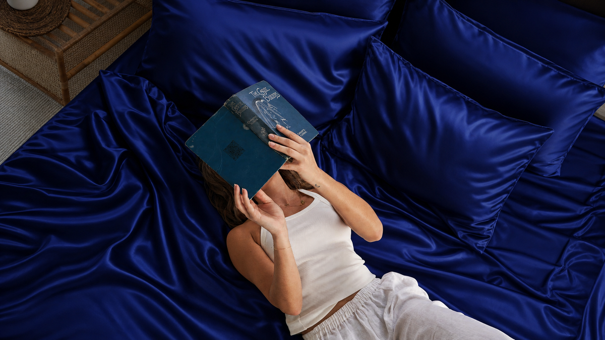 Woman lying on Navy Blue silk bedding holding an open book over her face