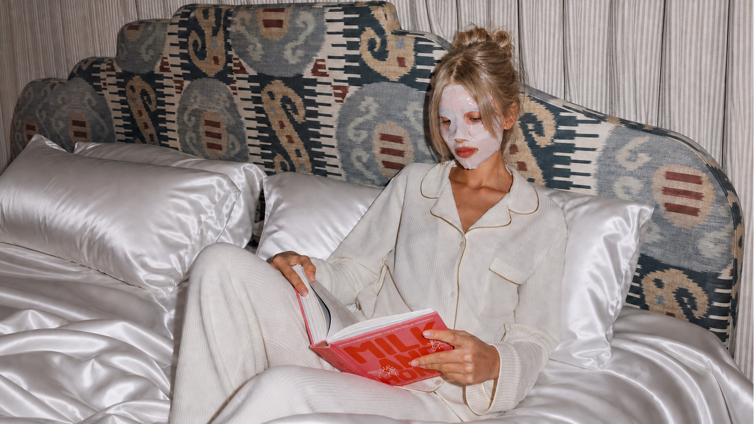 Woman with a face mask reading a book against Platinum Silver silk pillows in bed
